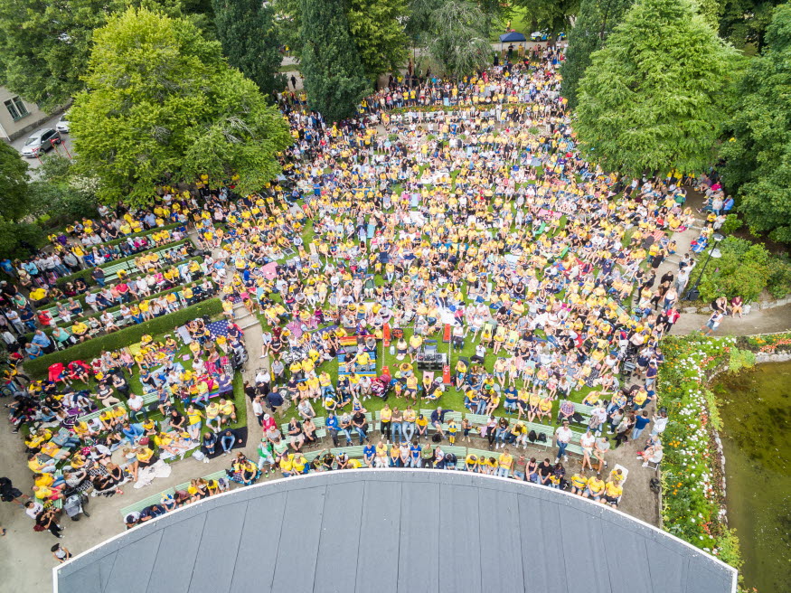 Folksamling i stadsparken med människor i gula och blå tröjor. 