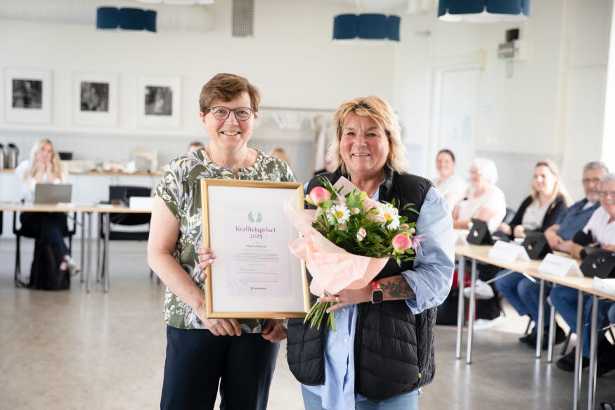 Två personer med blomsterbukett och diplom.