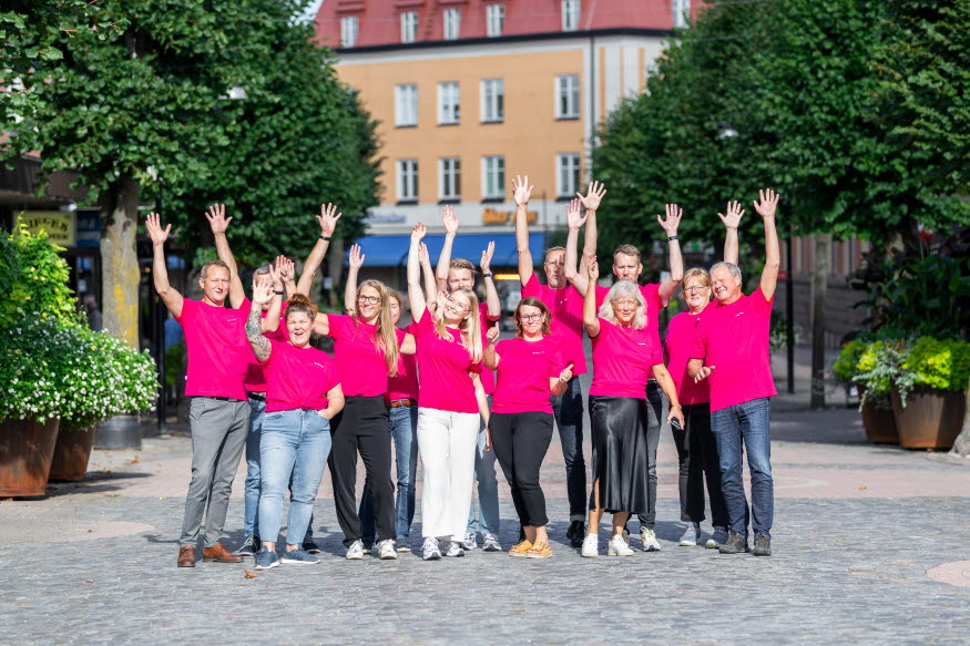 Flera tjänstepersoner från Katrineholms kommun iklädda rosa tshirts står på Köpmangatan i Katrineholm och ser glada ut.