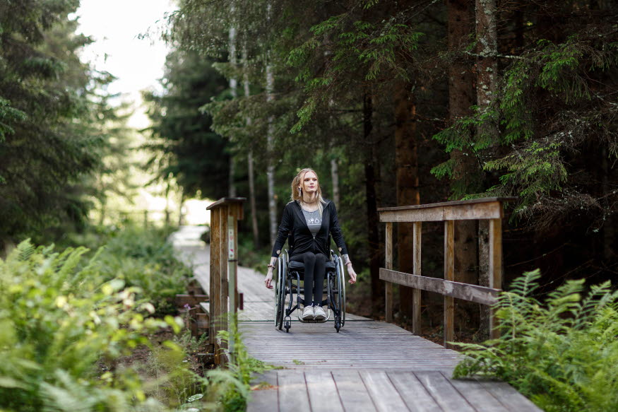 Person som sitter i rullstol njuter av en vistelse i Forssjö friluftsområde. Personen åker på en tillgänglighetsanpassad vandringsled.