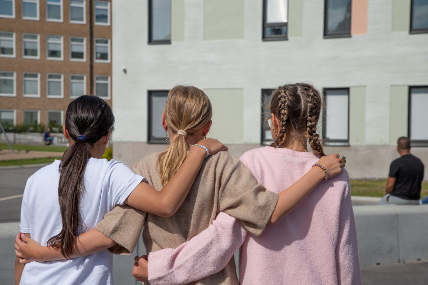 Tre ungdomar utanför en skola. 