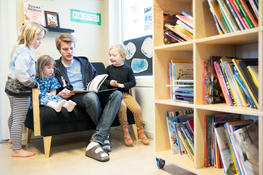 En förskollärare läser för några barn. Intill står en bokhylla. 