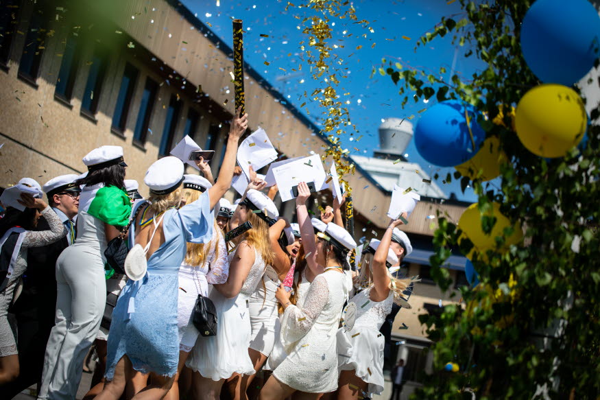 Festklädda studenter jublar med kuvert i handen.