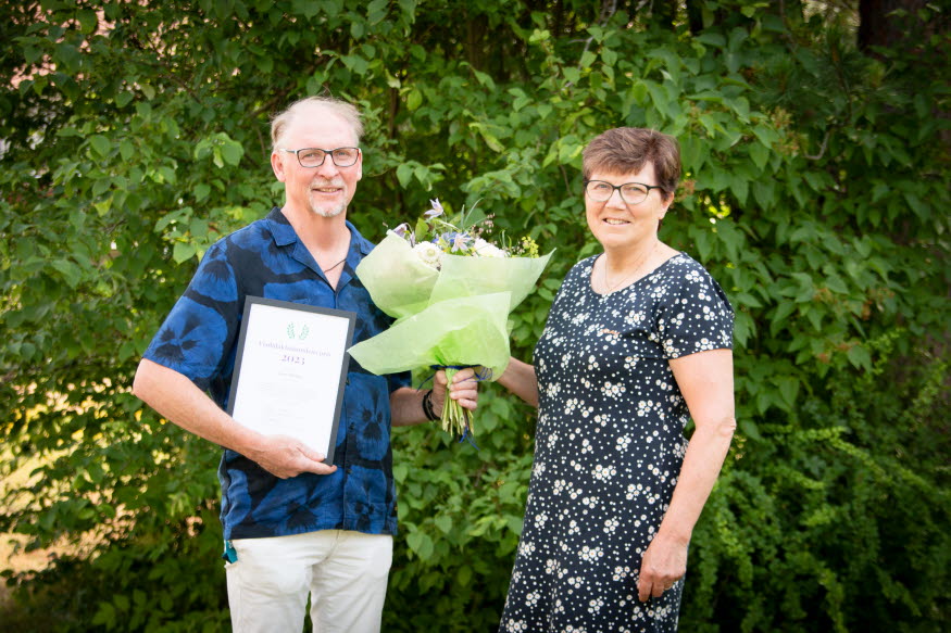 Två personer grönskan med diplom och blommor. 