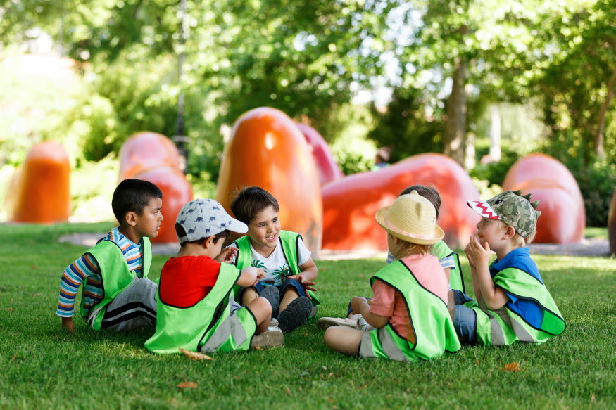 Barn i stadsparken i Katrineholm. De sitter i en ring på en gräsmatta och skrattar. 