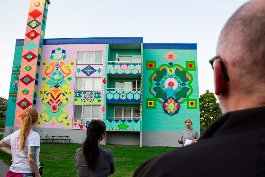Flera personer tittar på en husfasad som är målad i olika former och färger