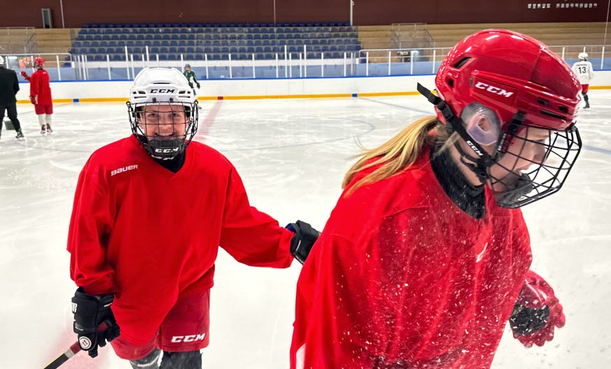 Två hockeytjejer i röda tröjor, i en ishall. 