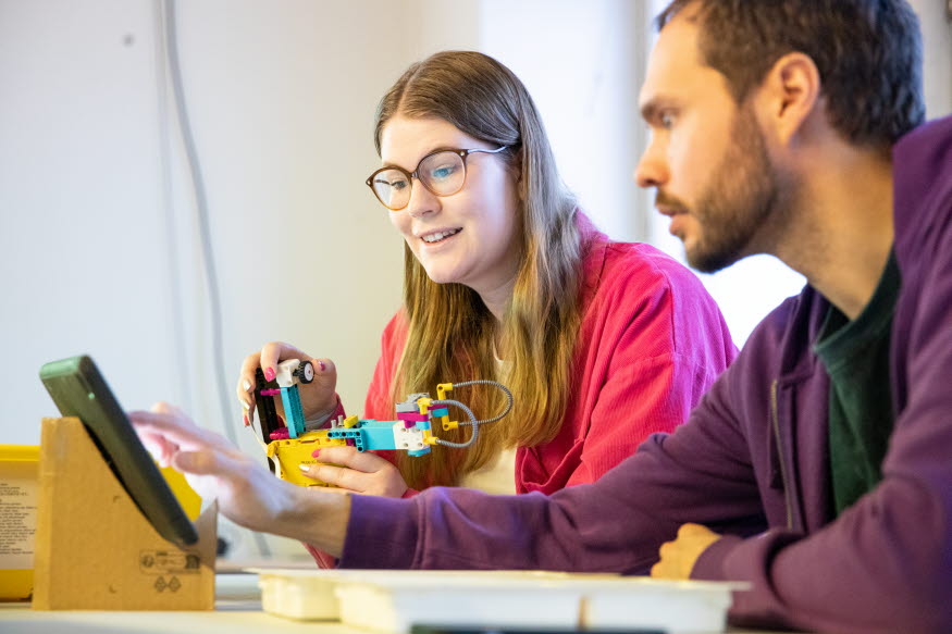 Två personer bygger lego och knappar på en läsplatta. 