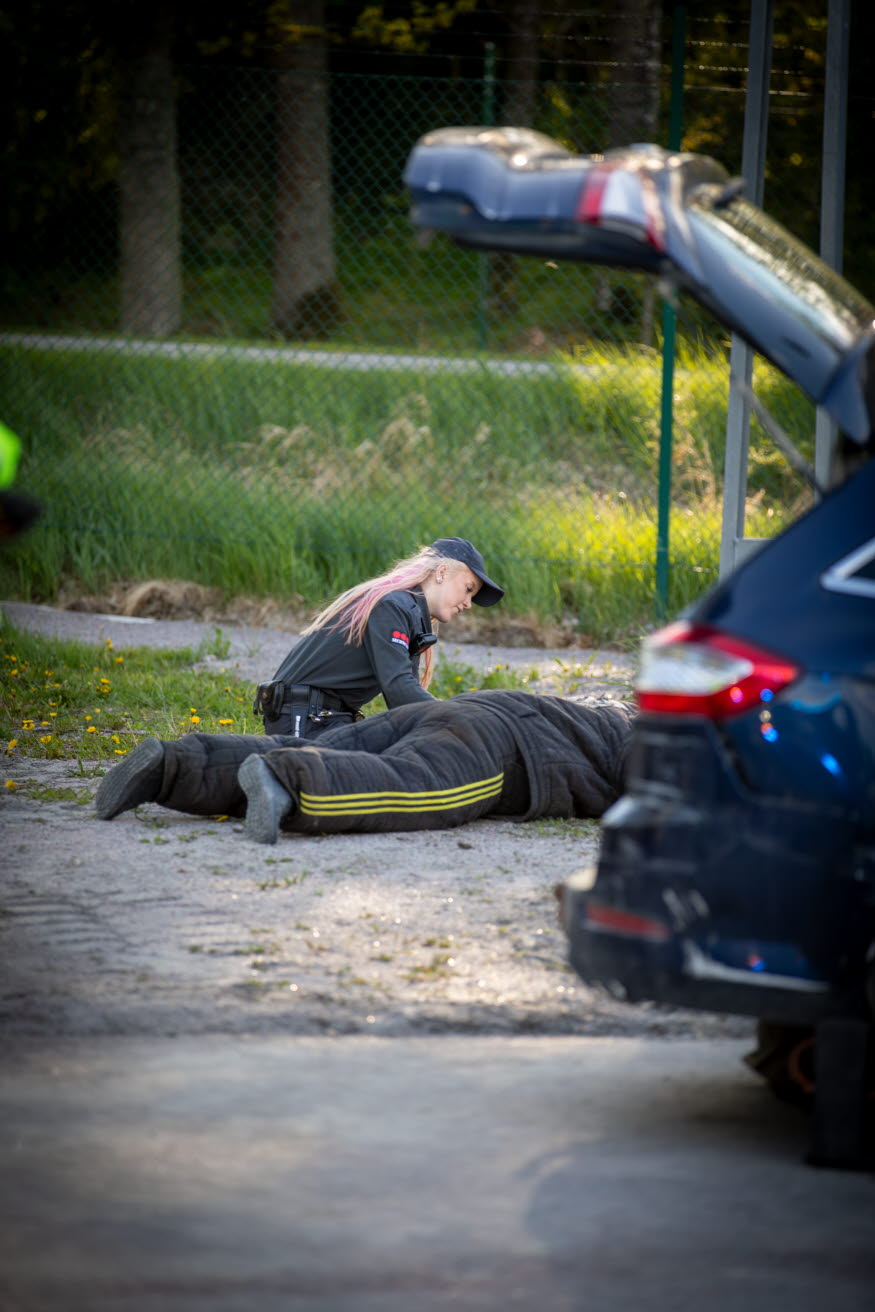 Mejja sitter hukad och hjälper en person som ligger på marken bakom en bil.