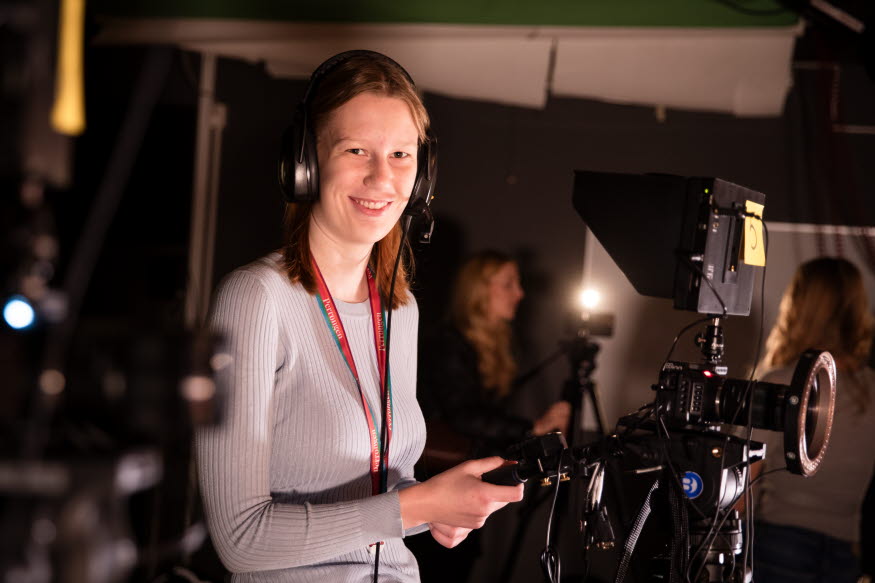 En person står bakom en filmkamera.