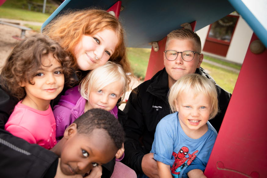 Två ungdomar tillsammans med barn i en lekpark.