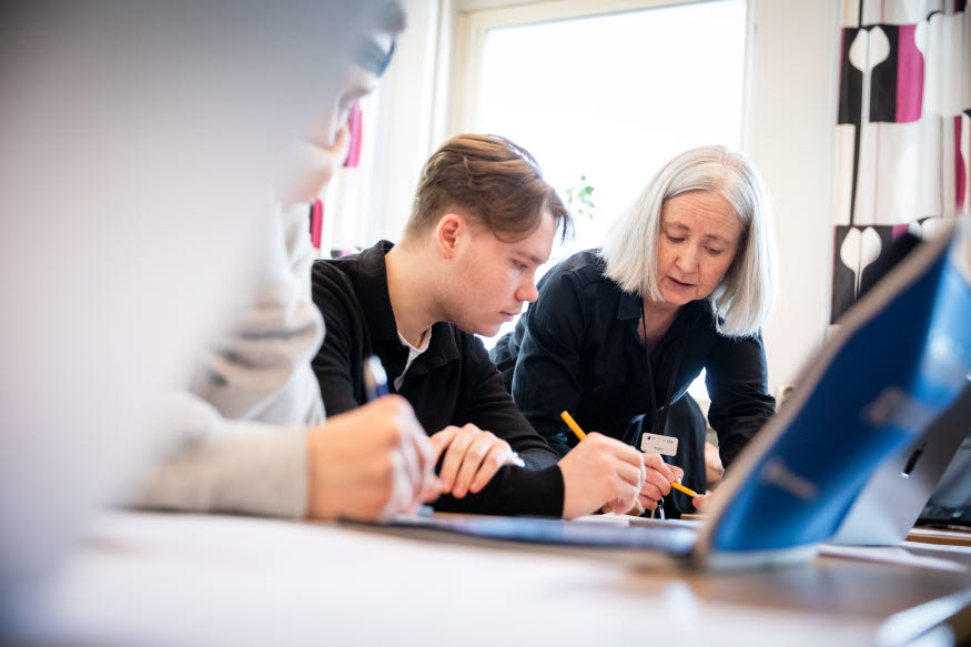 Elever samtalar med en lärare i ett klassrum. 