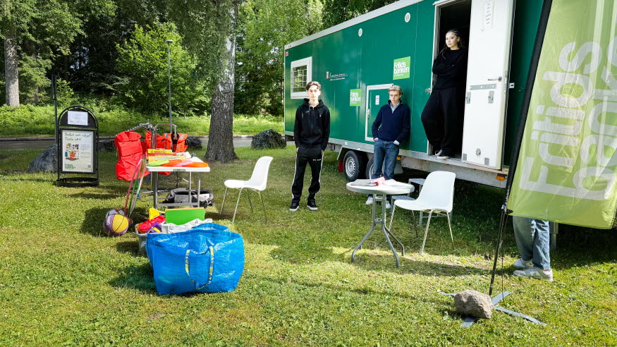 En grön vagn, bord med sportutrustning och några ungdomar. 