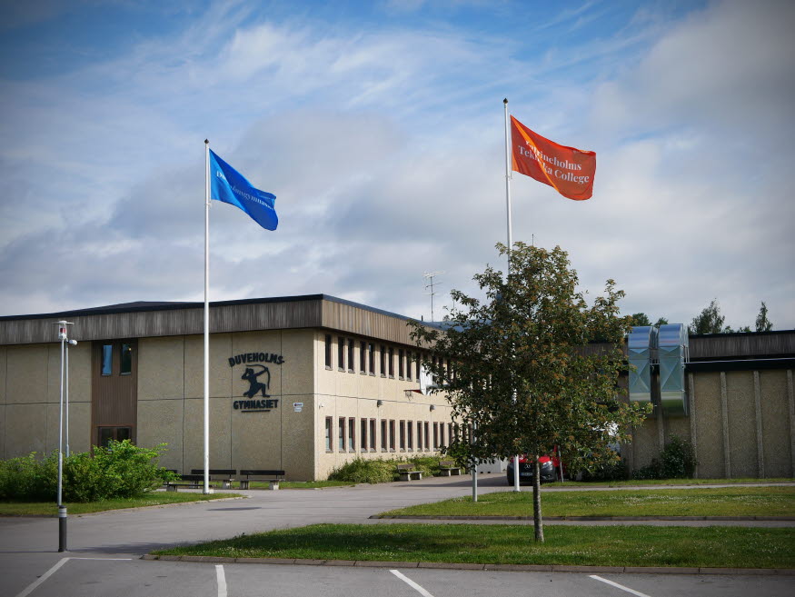 Duveholmsgymnasiets entré. Två flaggor vajar utanför, en blå och en orange. Foto: Maja Edsö