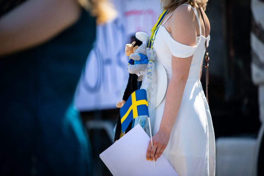 En student i vit klänning som håller i svenska flaggan.