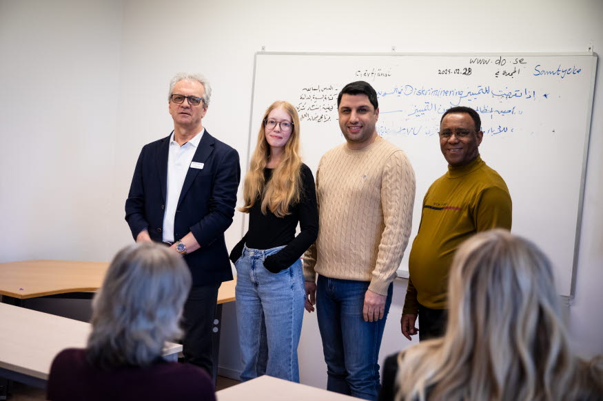 Fyra glada personer i ett klassrum. 