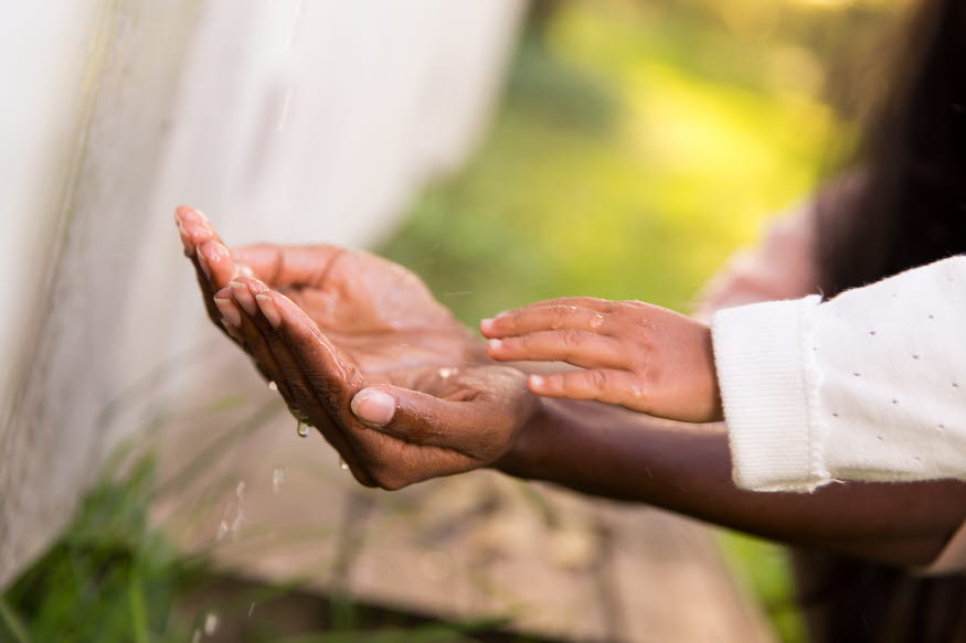 Två vuxenhänder och ett barns hand leker med vatten