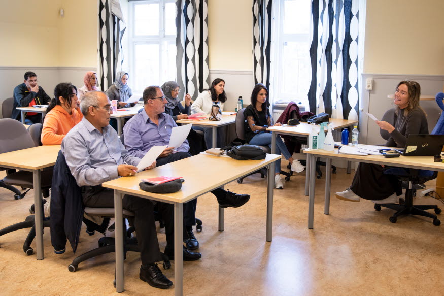 En grupp vuxna elever i ett klassrum med bänkar.