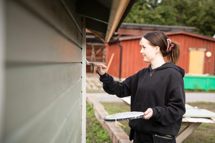 Ung person målar en fasad. 