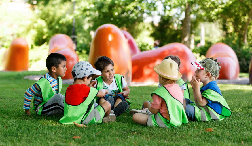 Barn sitter i Stadsparken och pratar. I bakgrunden syns konstverket Kreaturstorg av Monika Gora.