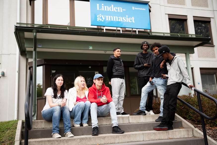 Sju personer sitter i en trappa framför en byggnad. 