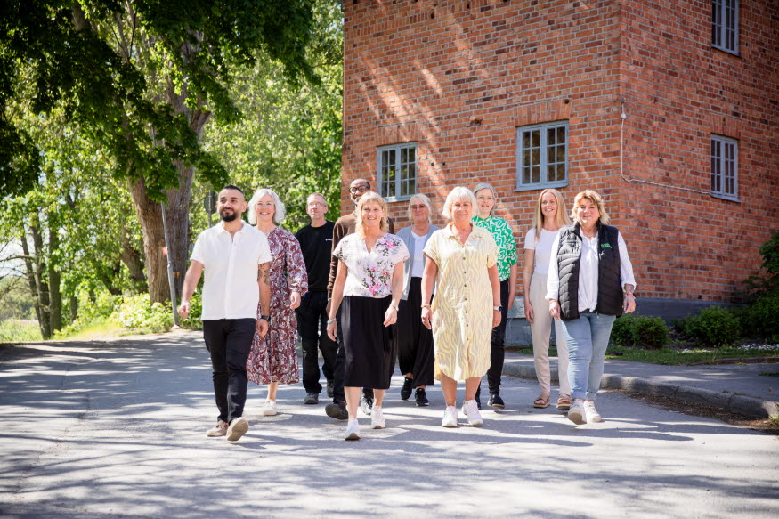 Gruppbild i grönskande miljö med en röd tegelbyggnad.