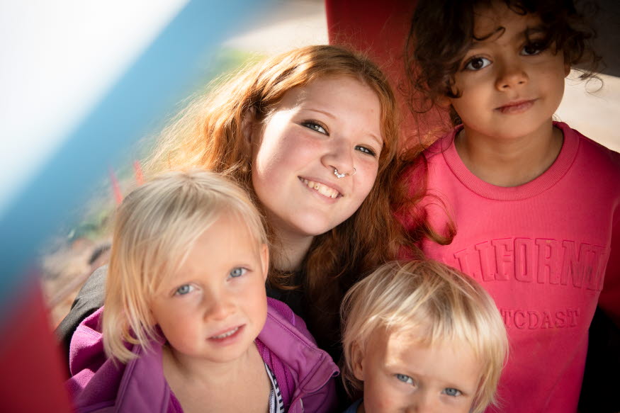 En ung person tillsammans med några barn i en lekpark. 