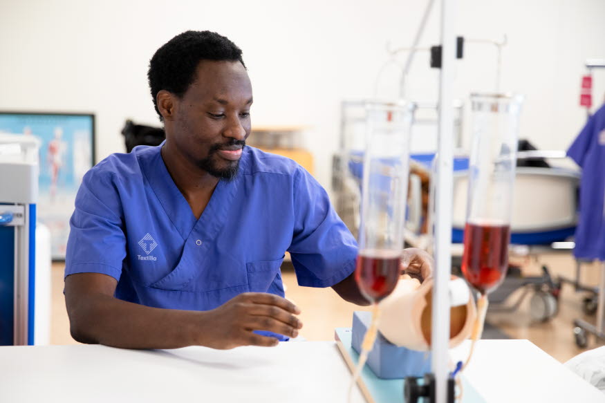 En person i blå vårdkläder i ett klassrum.