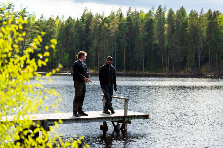 Två personer står på en brygga och fiskar. 