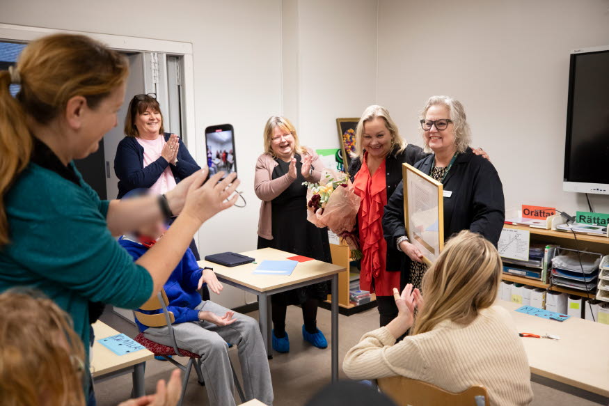 Fyra glada personer med diplom och blombukett, medan en annan tar bild med telefonen. 