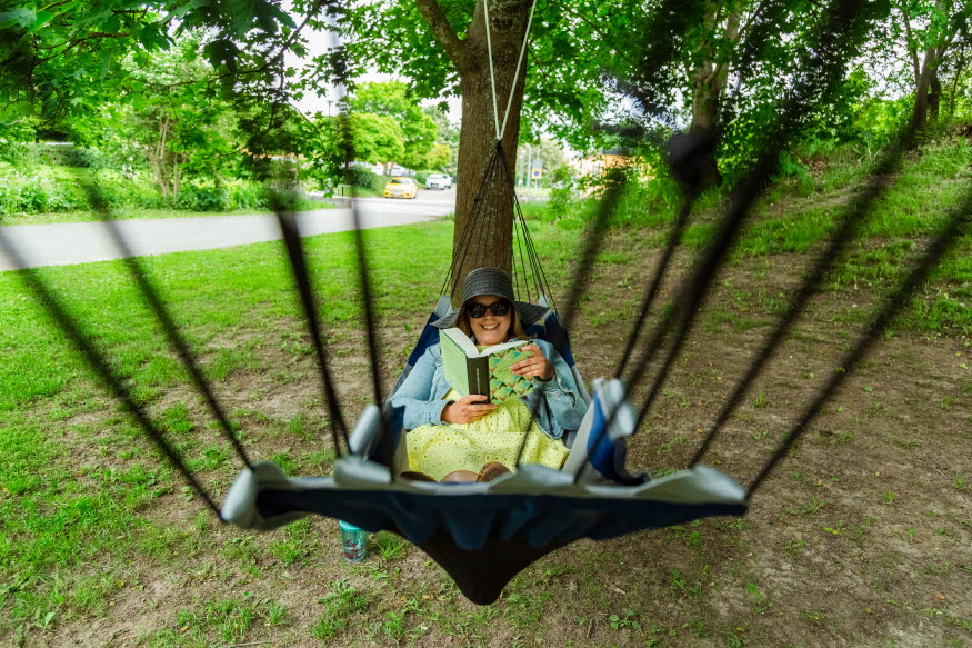 En person ligger i en hängmatta och läser en bok.