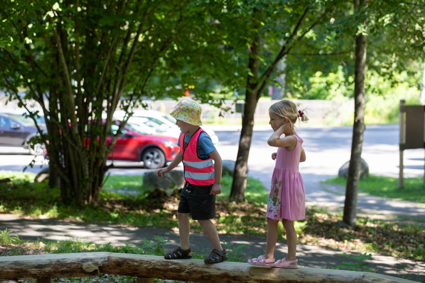 Två barn vandrar på en balansgång. Det ena barnet har shorts och gul hatt, det andra barnet har en rosa klänning.