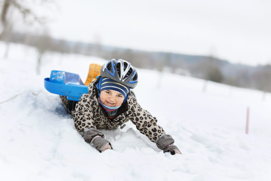 Ett barn leker i snön med en pulka